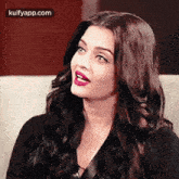 aishwarya rai is sitting on a couch with her mouth open and wearing a black top .