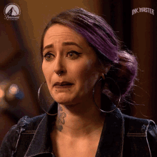 a woman with purple hair and hoop earrings is a contestant on ink master