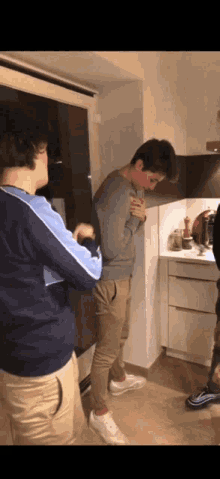 a man in a gray sweater stands in a kitchen with his hands on his chest