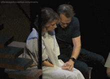 a woman in a hospital gown sits next to a man in a green shirt