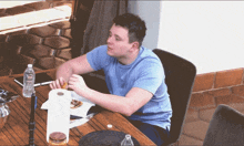 a man in a blue shirt sits at a table eating a sandwich