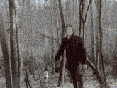 a man in a black coat walking through a forest