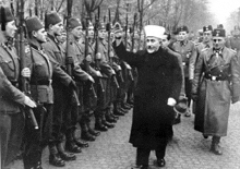 a black and white photo of a man standing in front of a row of soldiers
