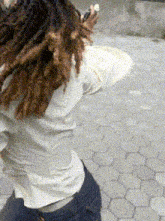 a person with dreadlocks and a white shirt is standing on a brick sidewalk .