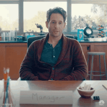 a man is sitting at a desk with a sign that says manager