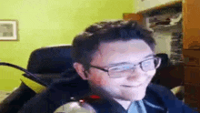 a man wearing glasses and a black jacket is sitting in a chair .
