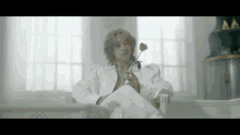 a man in a white suit holds a rose in his hand