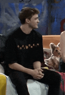 a man wearing a black shirt that says golden is sitting on a couch