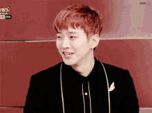 a young man with red hair is smiling in front of a red wall with 2pm written on it