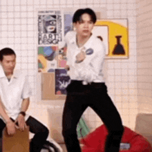 a man is dancing in a room while another man sits on a couch .