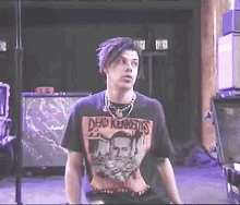 a young man wearing a dead kennedys t-shirt stands in a dark room