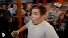 a man is making a funny face while holding a glass in front of a crowd of people .
