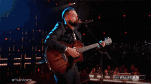a man is singing into a microphone while playing a guitar on stage