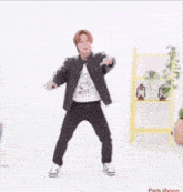 a man in a black jacket and black pants is dancing in front of a yellow shelf