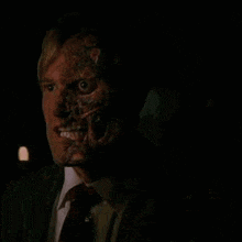 a man in a suit and tie with a scary face is looking at the camera .