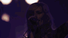 a woman singing into a microphone with purple lights in the background