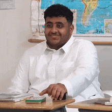 a man in a white shirt sits at a desk in front of a map of the world