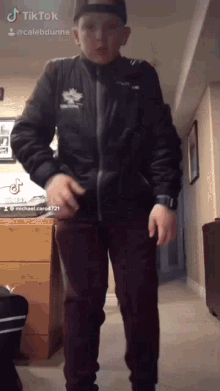 a boy wearing a black jacket with a maple leaf on it is standing in a hallway