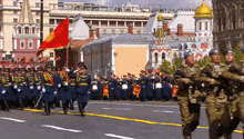 a group of soldiers marching in a parade with a red flag in the foreground