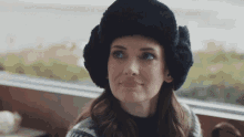 a woman wearing a black fur hat and ear muffs looks out a window