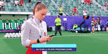 a woman stands on a soccer field looking at her phone .