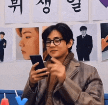 a young man wearing glasses is holding a cell phone