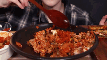a person is eating food with a wooden spoon in a black bowl