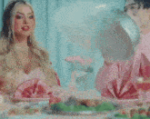 a woman in a pink dress is sitting at a table with plates of food and a man in a pink shirt .