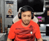 a man wearing headphones and a red shirt is sitting in a chair in front of a tv .