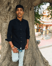 a young man leaning against a tree with a phone in his hand