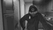 a black and white photo of a man wearing a hoodie and a hat with a skull and the letter t on it