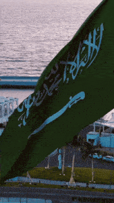 a green flag with arabic writing on it is flying in front of the ocean