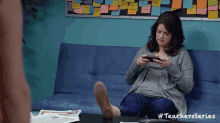 a woman is sitting on a couch with her feet on a table looking at her phone .