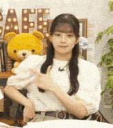 a young girl is sitting in front of a teddy bear and giving a thumbs up .
