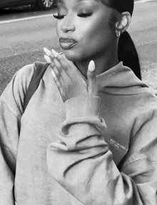 a black and white photo of a woman wearing a hoodie and holding her hand to her chest .