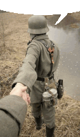 a man in a military uniform is holding another man 's hand while walking near a river
