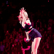 a woman in a crop top and shorts holds a microphone on a stage