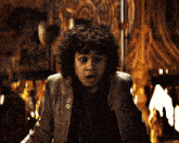 a young boy with curly hair is wearing a jacket with a patch that says ss on it