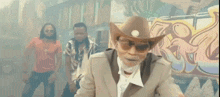 a man with a beard and sunglasses is wearing a cowboy hat and a suit .