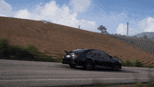 a black car is driving down a road in front of a hill