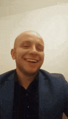 a bald man in a suit and black shirt is smiling with his eyes closed in a video taken by vida