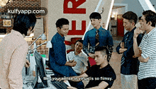 a group of men are standing around a man sitting at a desk in front of a computer screen .