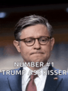 a man in a suit and tie is wearing glasses and says number # 1 trump ass kisser .