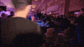 a crowd of people are gathered in a room with a purple light shining on them