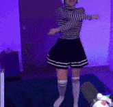 a woman in a striped shirt and shorts is dancing in front of a purple wall ..