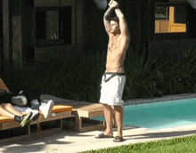 a shirtless man stands in front of a pool with his arms in the air