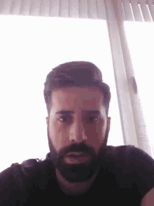 a man with a beard wearing a black shirt is looking at the camera