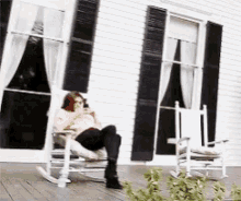 a woman is sitting in a rocking chair on the porch of a house