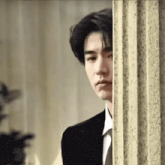 a young man in a suit and tie is peeking out from behind a column .