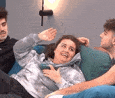 a woman is laying on a couch with two men and holding a bowl .